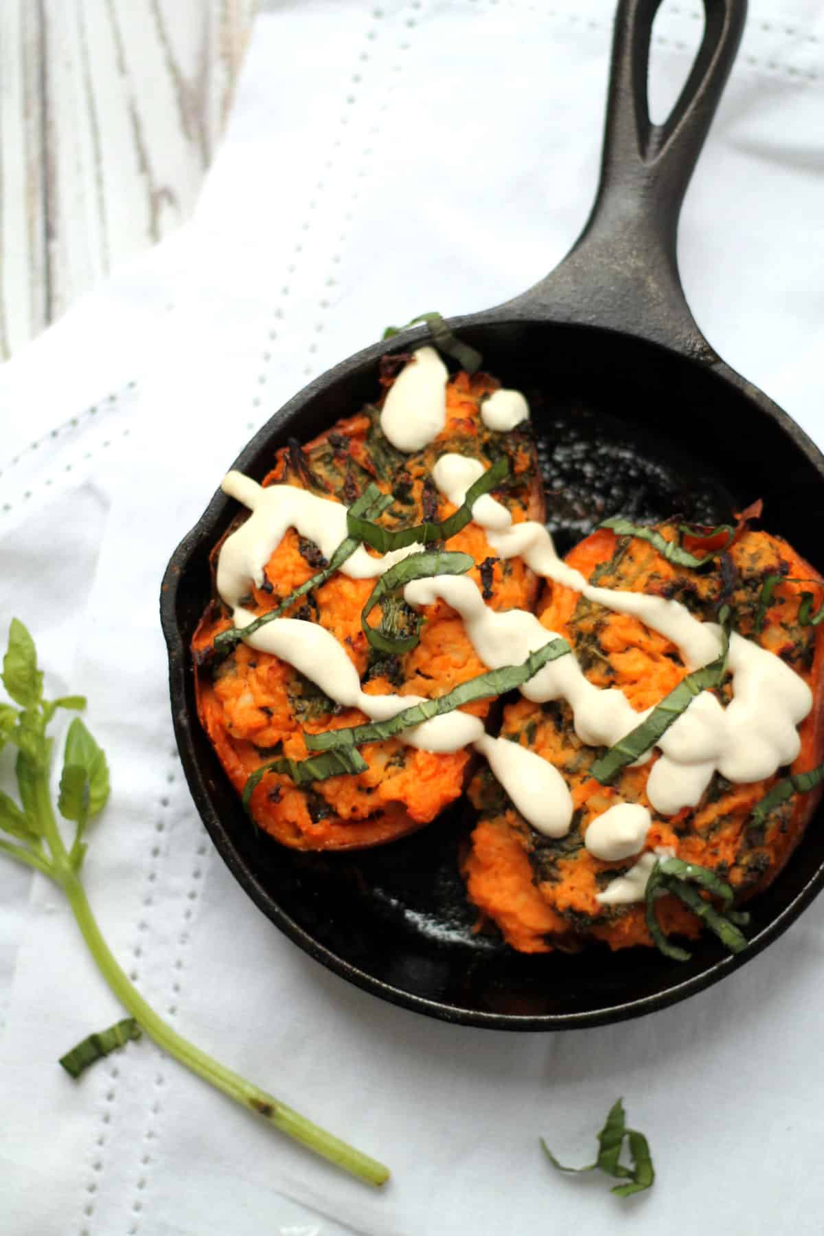 Overhead view of stuffed sweet potatoes with goat cheese and kale placed on an iron skillet pan.
