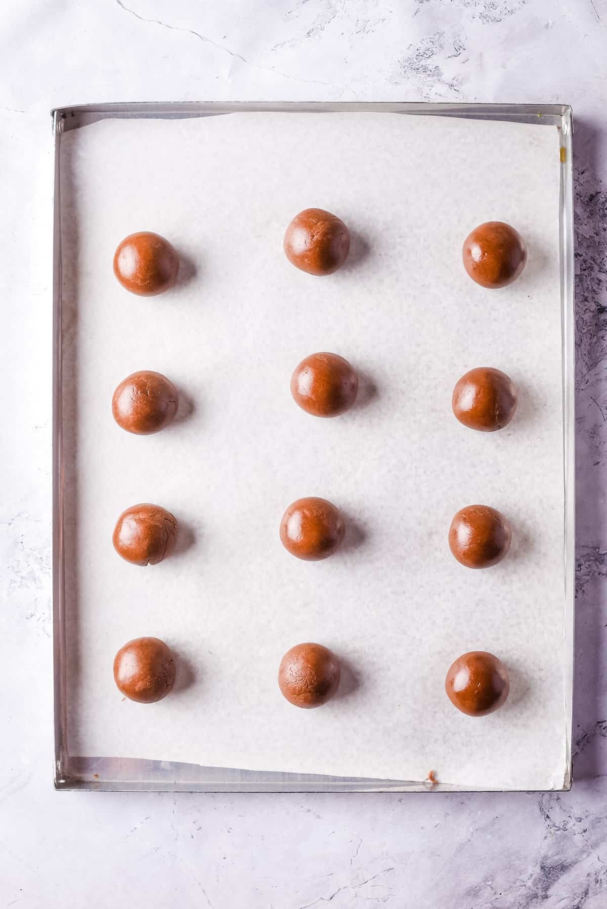 Overhead view of Nutella cookie dough balls on baking sheet lined with parchment paper.