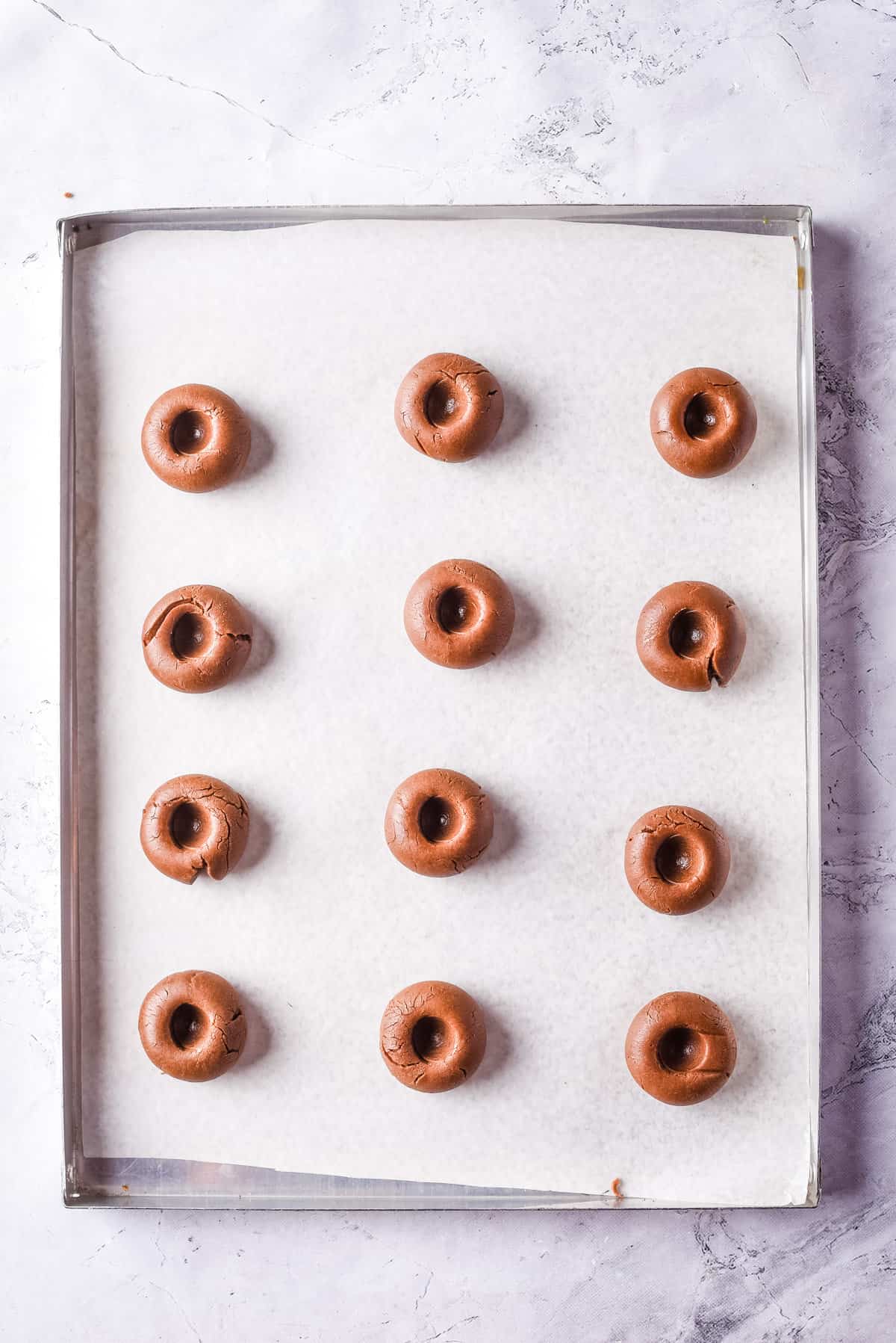 Overhead view of baking sheet with cookie dough balls pressed down to create wells in them.