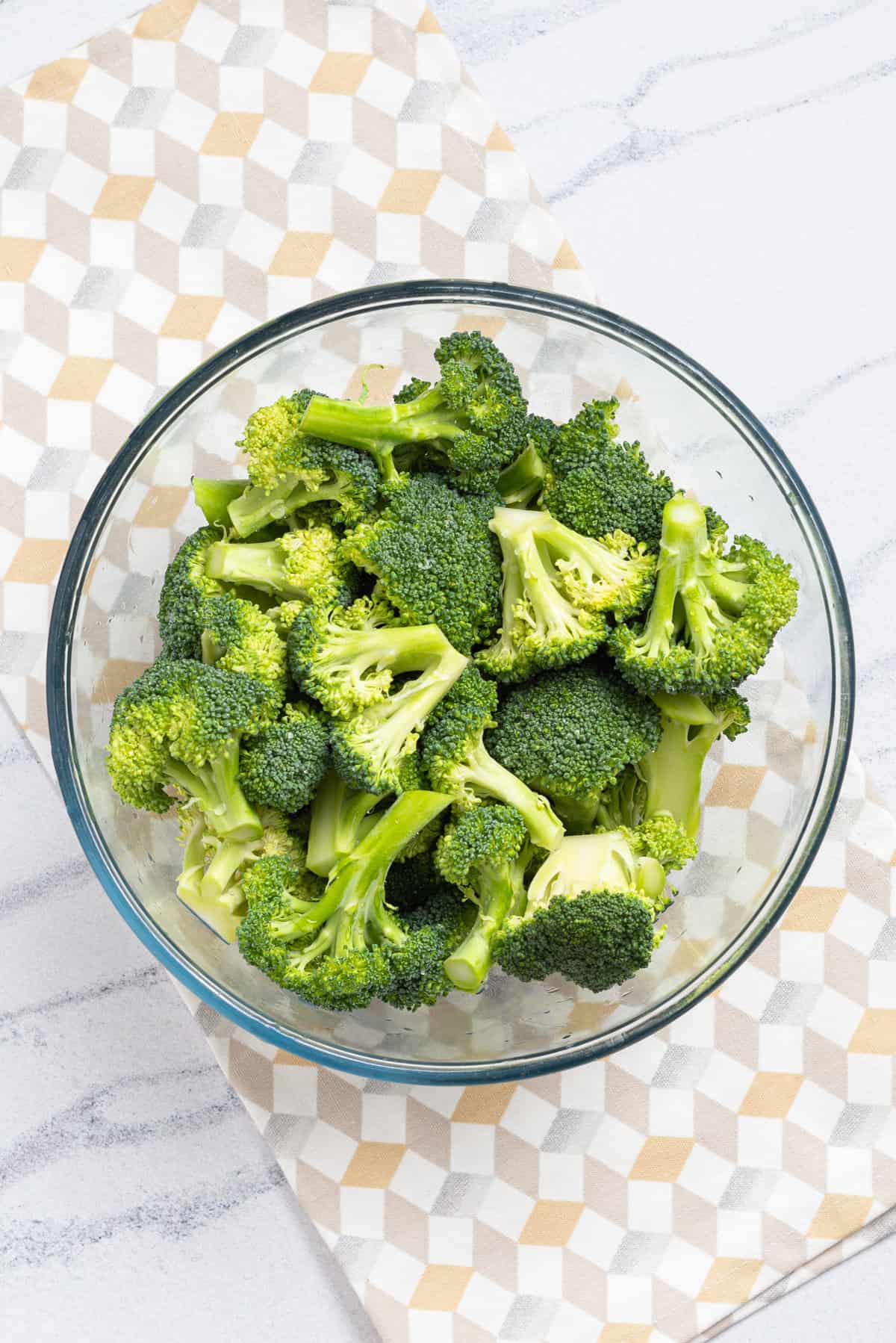 An overhead image of broccoli florets in a clear bowl with water.