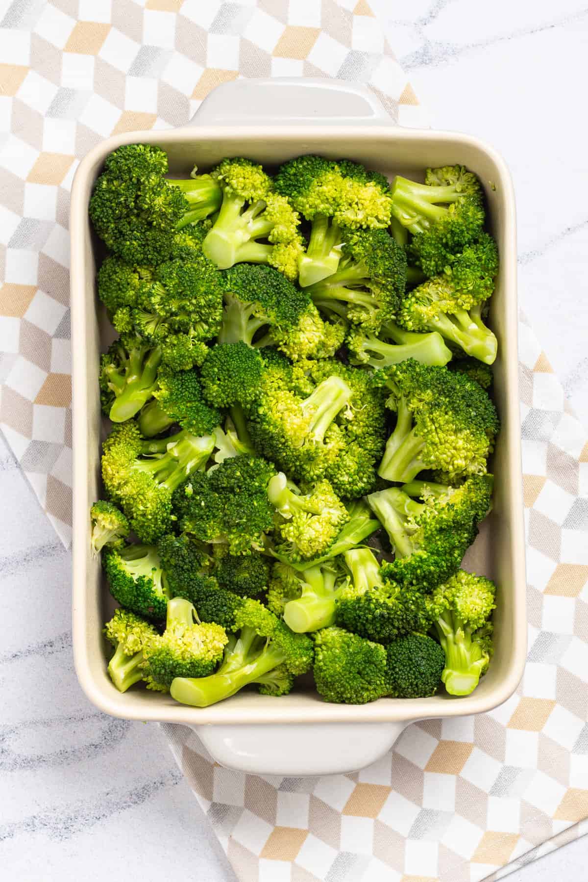 An overhead image of a white casserole dish filled with broccoli florets.