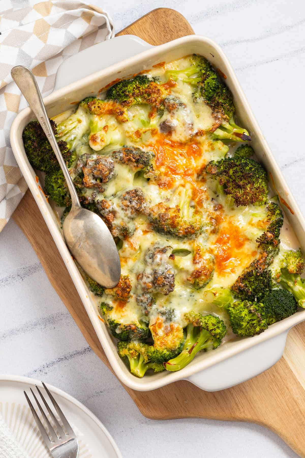 An overhead image of broccoli cheese casserole served in a white casserole dish with a spoon resting on the left side.