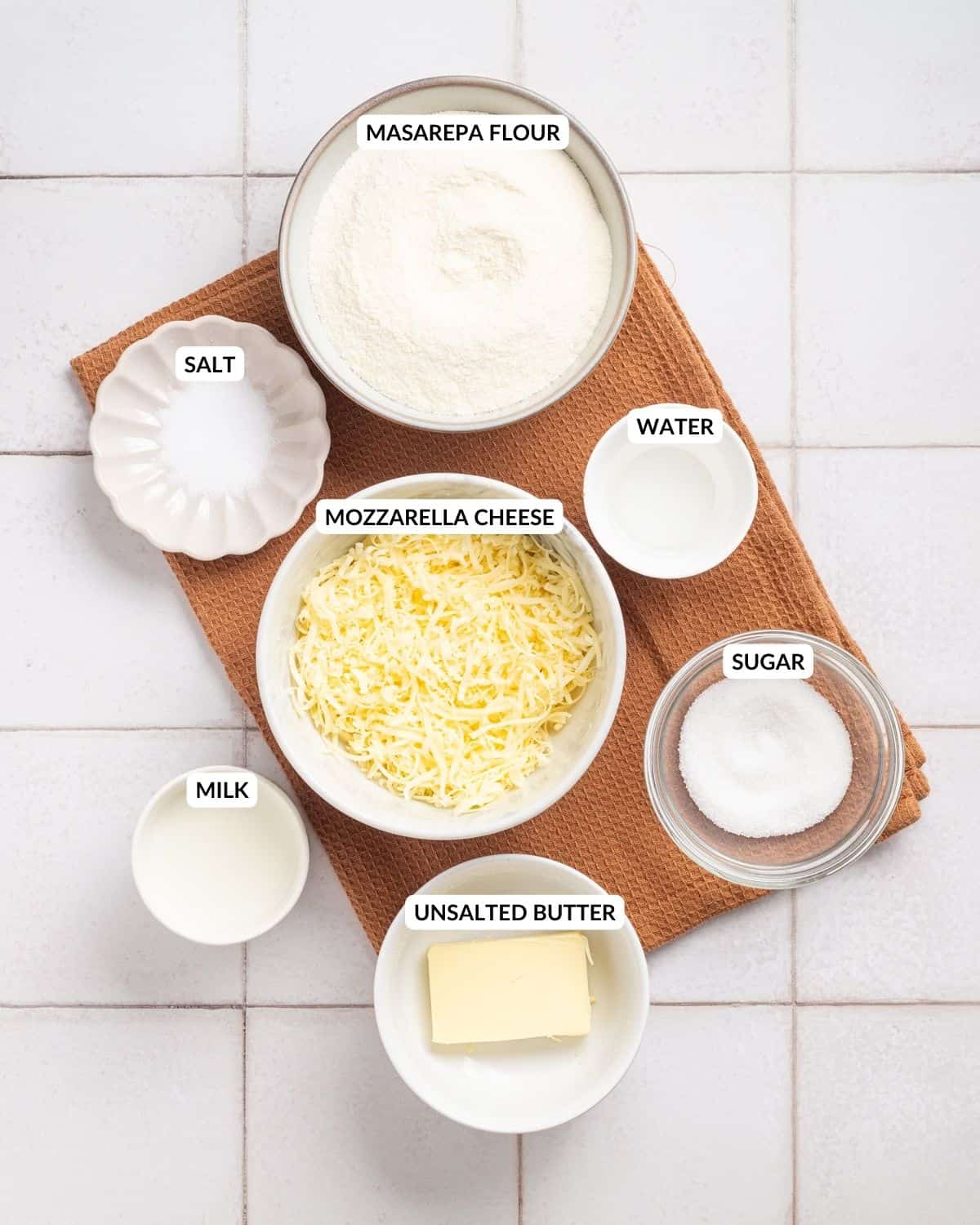 An overhead image of the ingredients of arepas con queso in separate containers with labels on each of them.