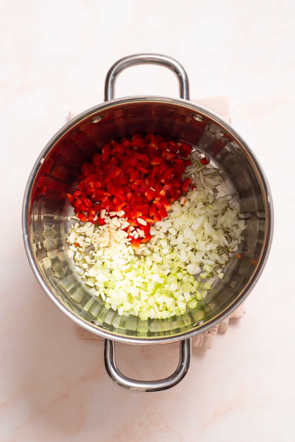 An overhead image of onion, celery, red bell pepper and garlic in a saucepan.
