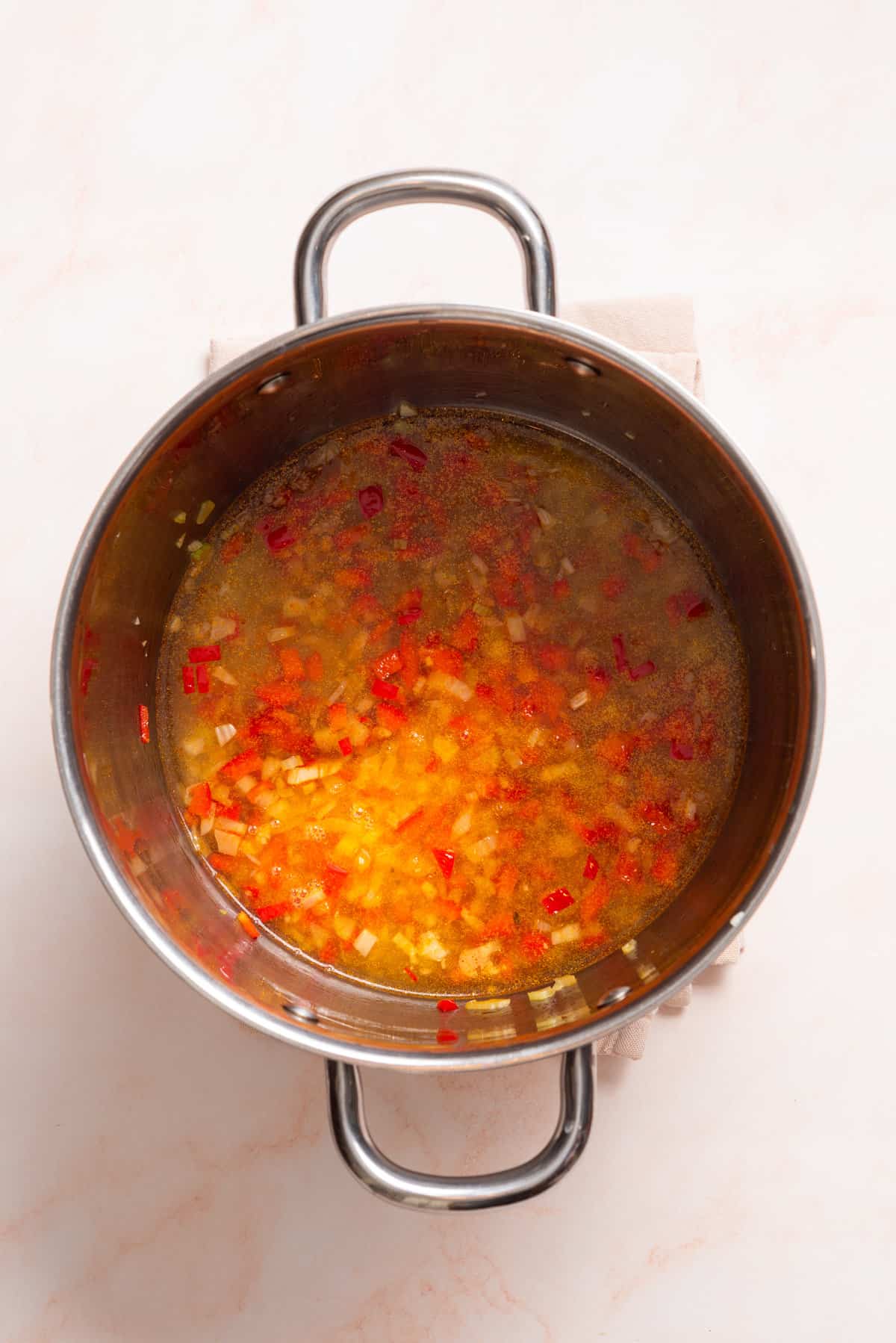 An overhead image of broth added to a saucepan.