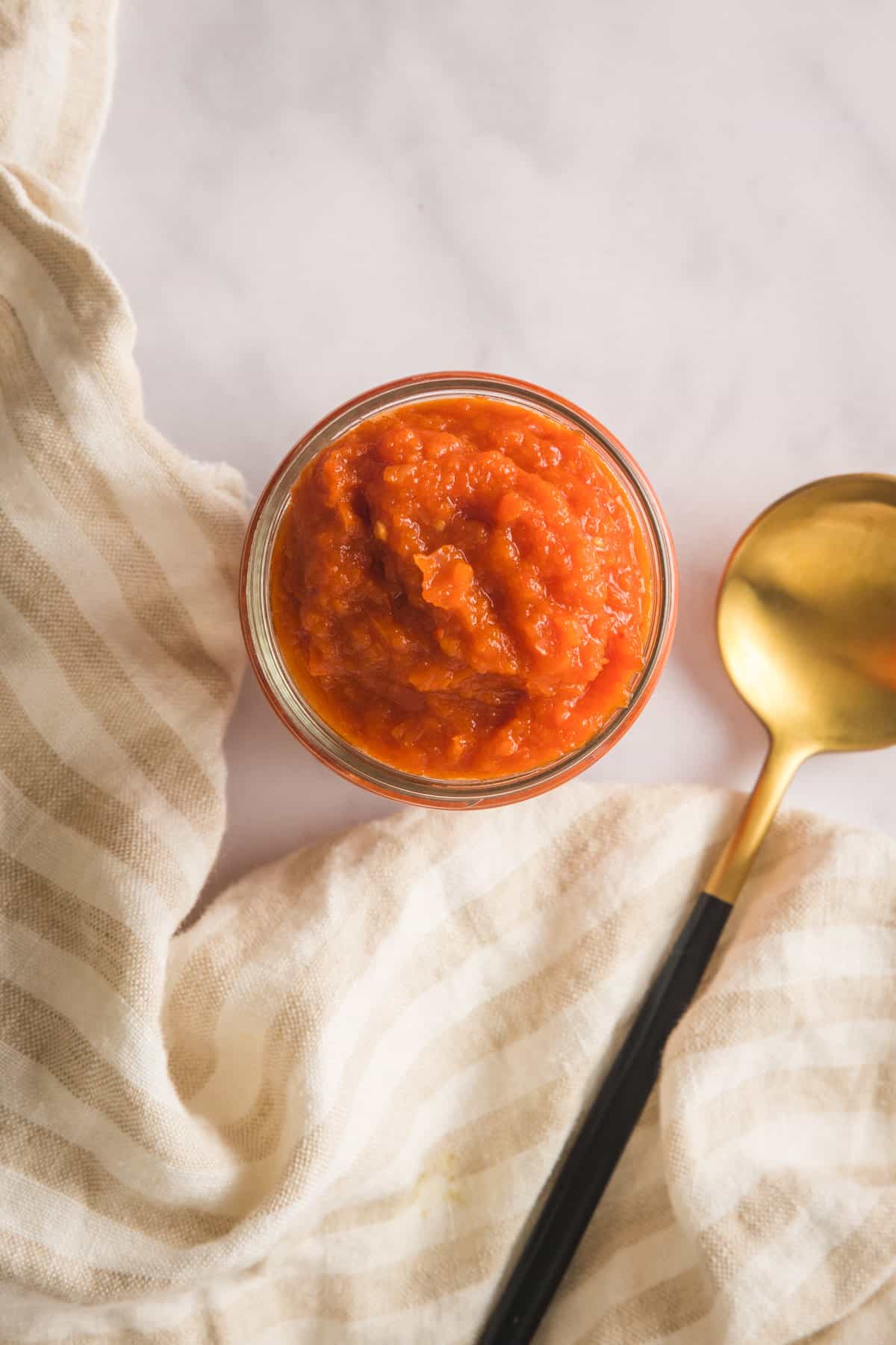 Overhead view of the sauce in a jar, with a golden black spoon on the side.