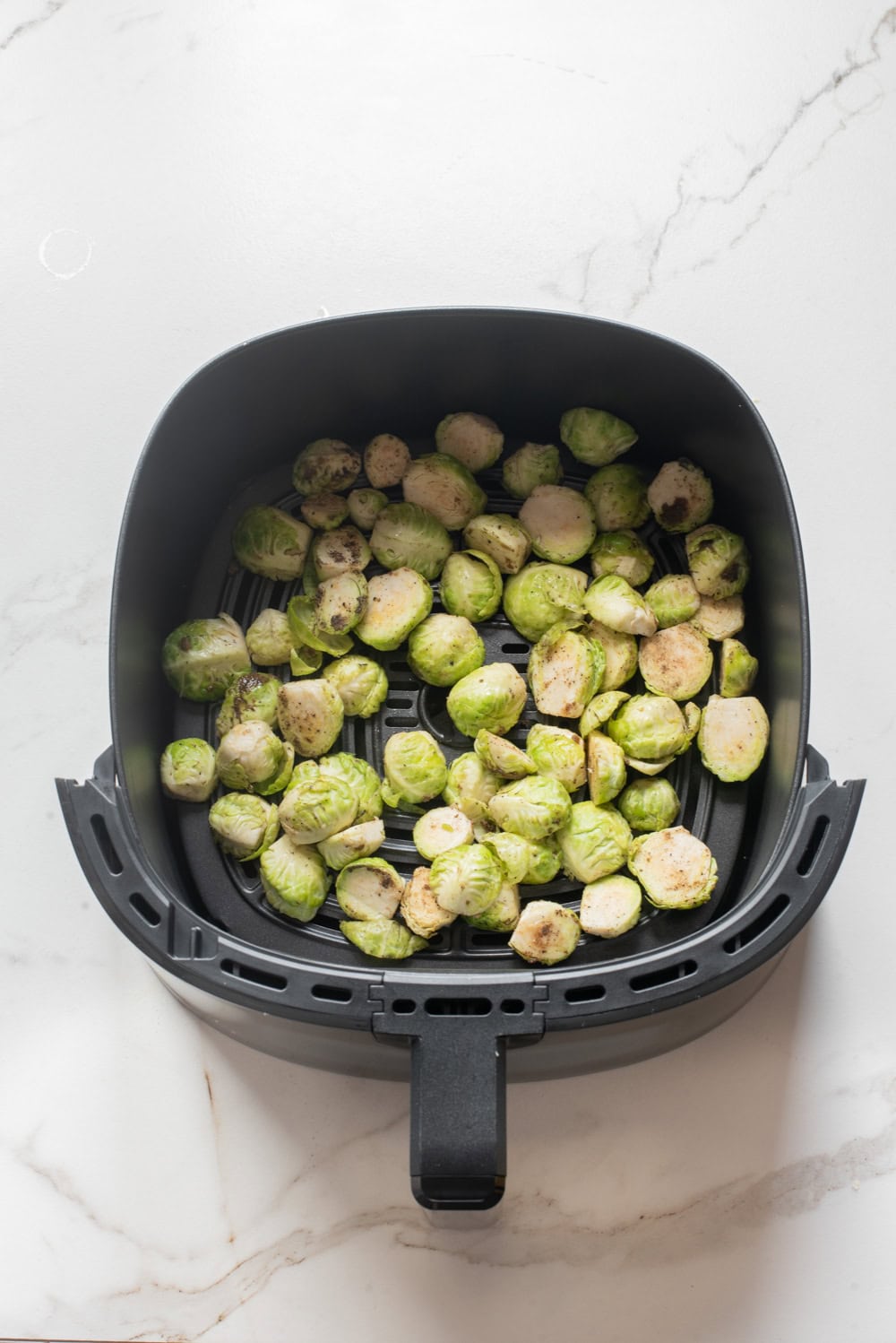 Seasoned Brussels sprouts arranged in an air fryer basket before cooking.