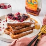 Close up of air fryer French toast slices on a white plate, with berries and powdered sugar topping