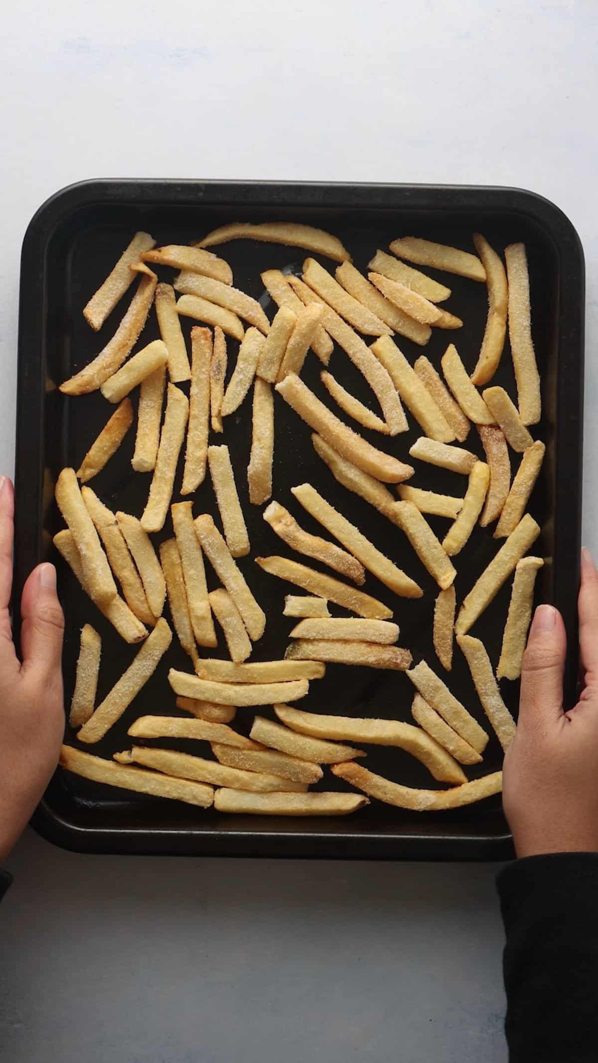 Overhead shot of holding air fryer tray with frozen fries.