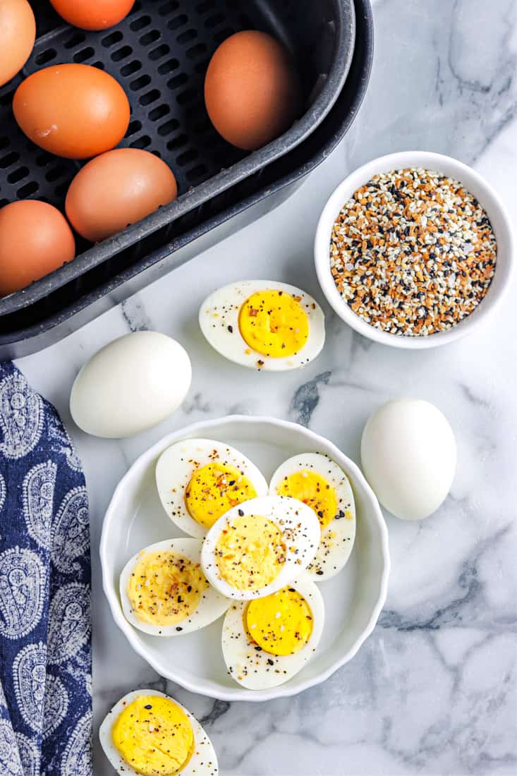 Overhead view of air-fried boiled eggs placed on a white plate and some eggs in the air fryer basket.