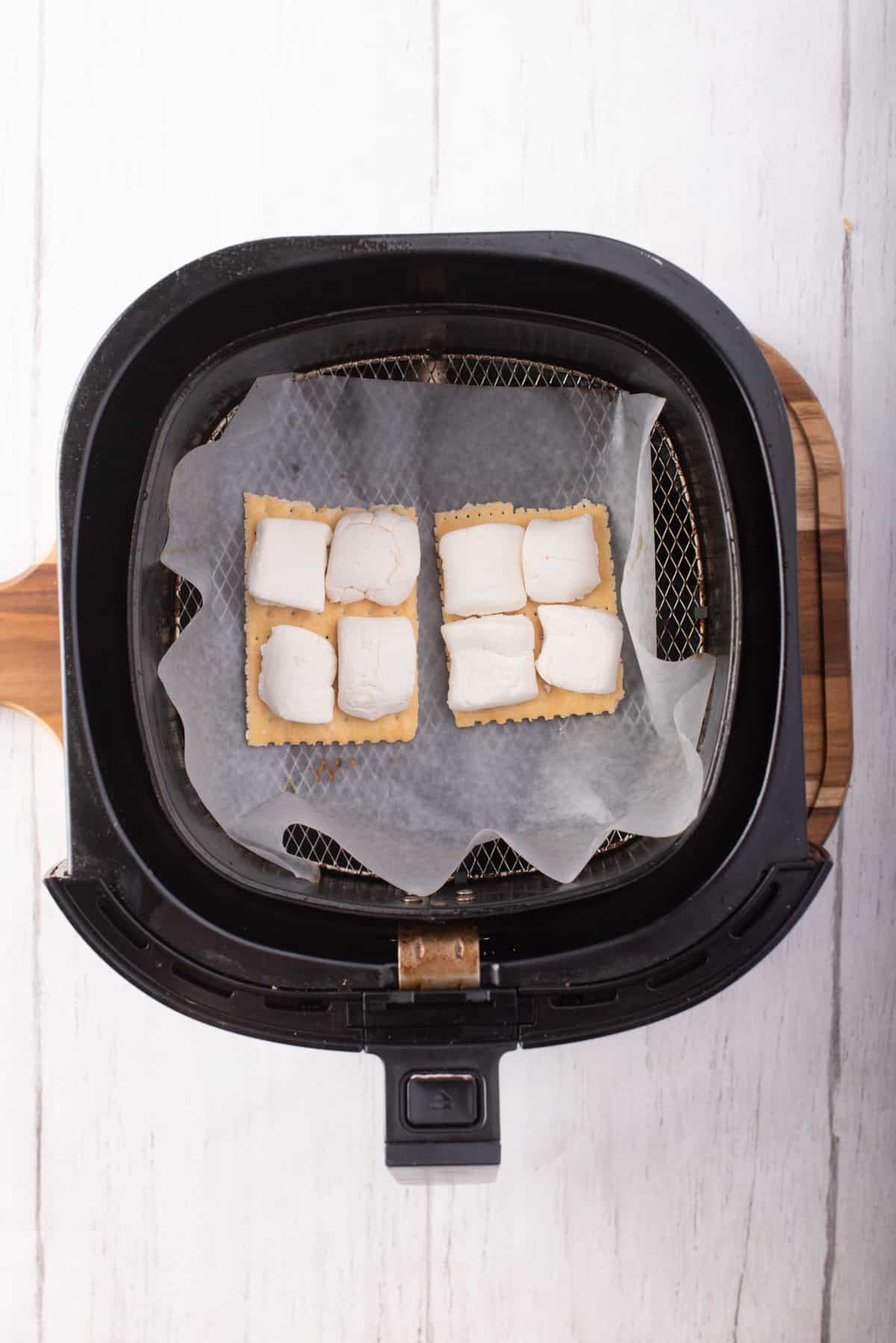 Overhead view of two Graham crackers with marshmallows cut in half on top, placed on the air fryer basket.