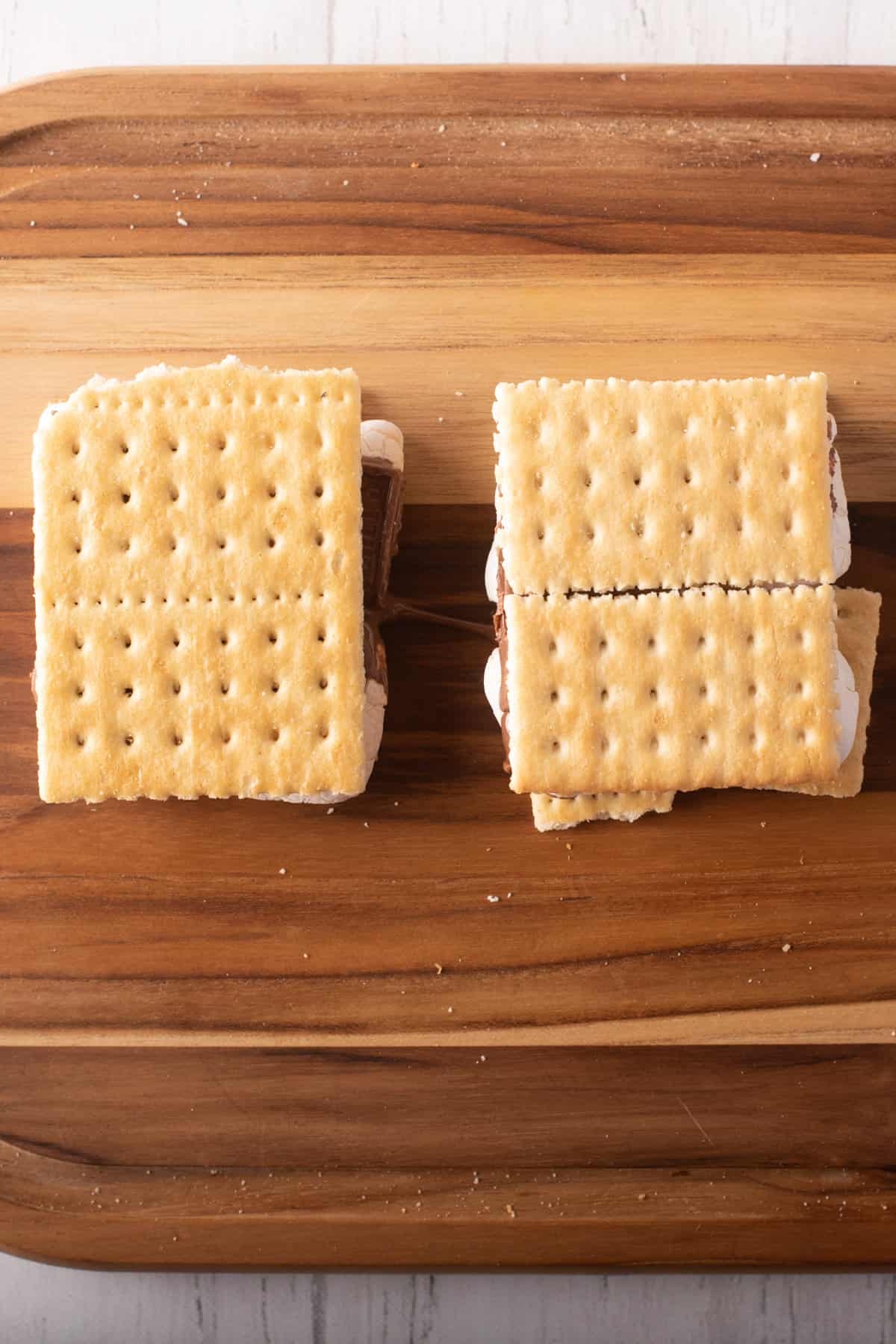 Overhead view of two Graham crackers with chocolate and marshmallow filling placed above a wooden board. 