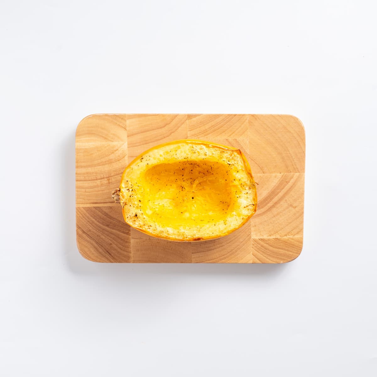 An overhead image of a fried spaghetti squash half, facing up on a cutting board.