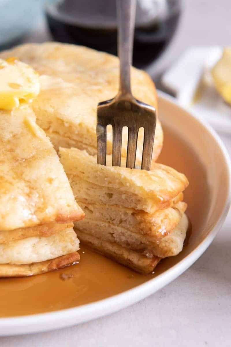 Close-up view of a fork getting several slices of air fried pancakes on a white plate.
