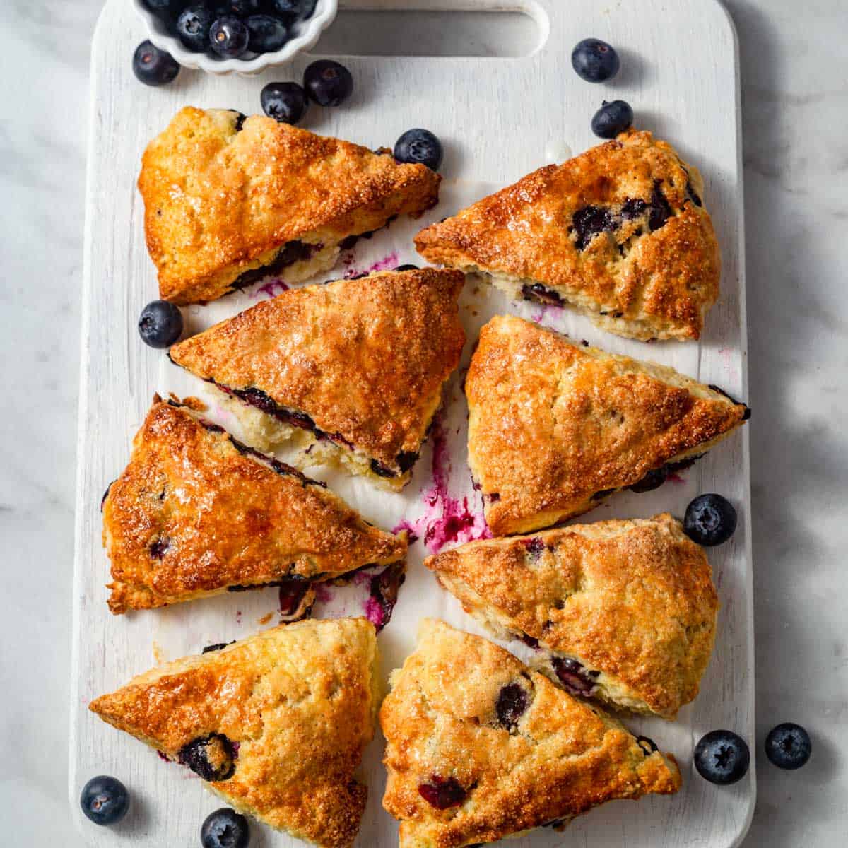 Overhead view of air-fried blueberry scones placed on a white plate along with fresh blueberries on them.