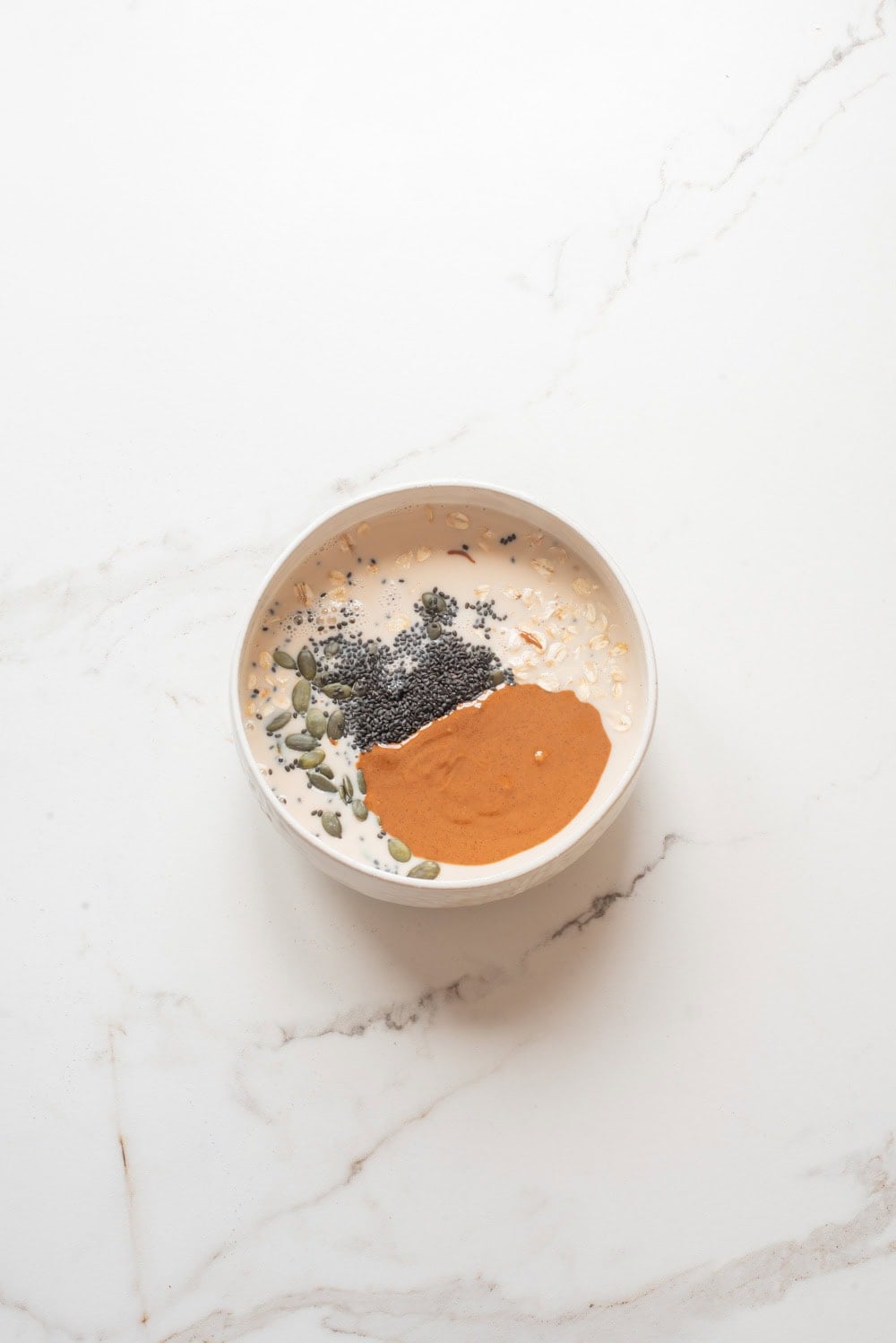 Almond butter, chia seeds, and pumpkin seeds. added to oats and milk mixture in a bowl.