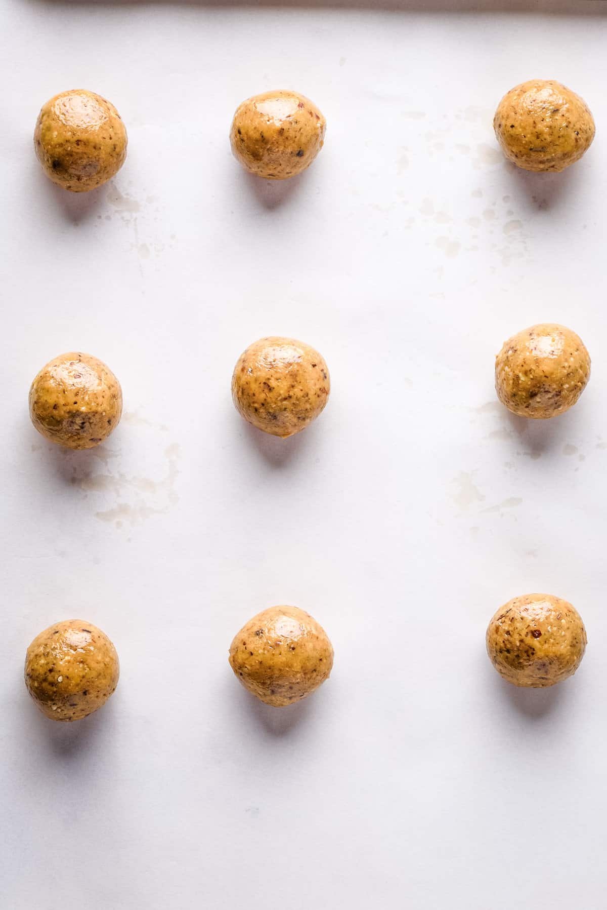 Overhead view of cookie dough balls on baking sheet lined with parchment paper.