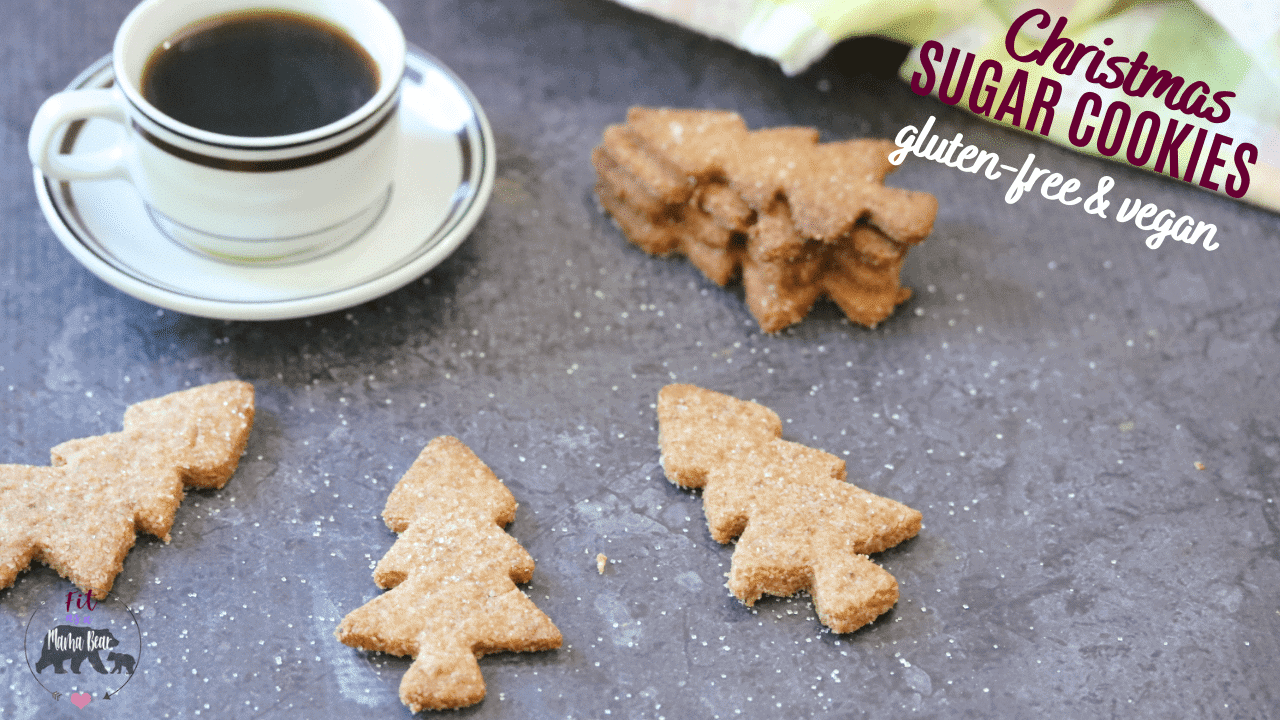 A straight view of healthy almond flour sugar cookies in Christmas tree shapes around the white mug full of coffee. 