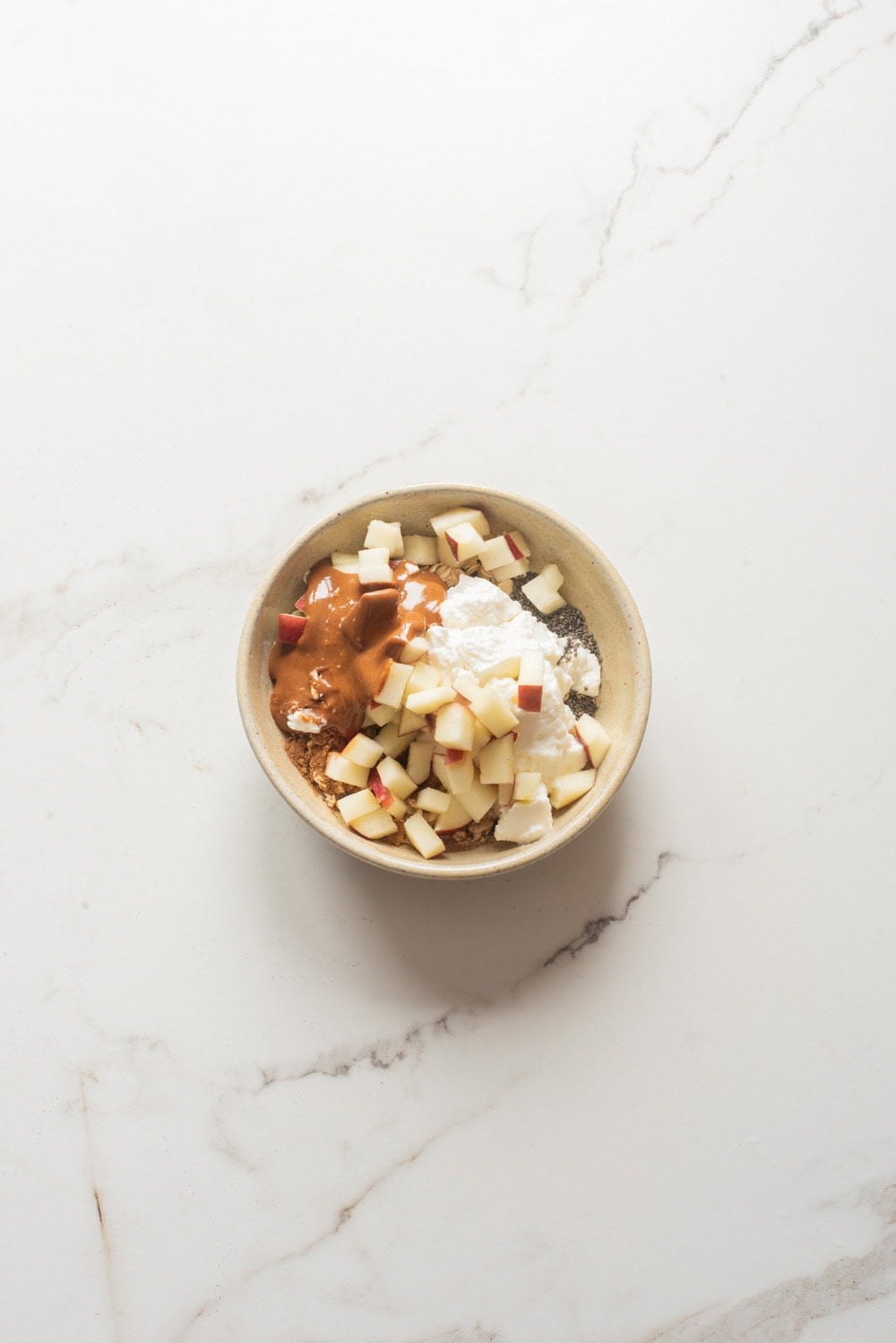 Overhead image of the ingredients of apple pie chia overnight oats added in a bowl.