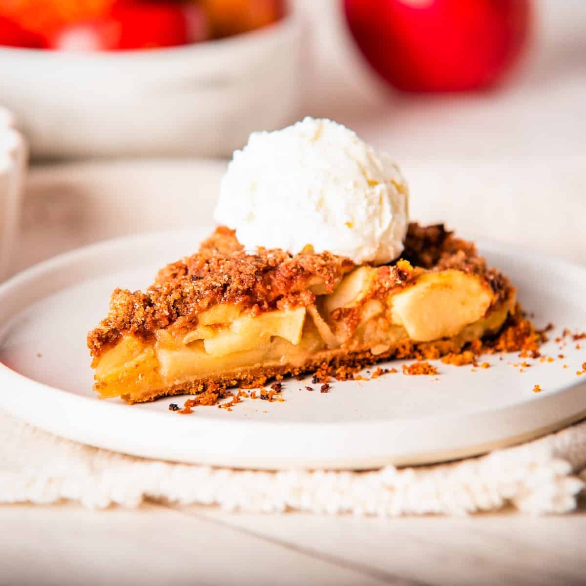 A close-up of a sliced apple pie with graham cracker crust on a white plate, topped with a scoop of vanilla ice cream. 