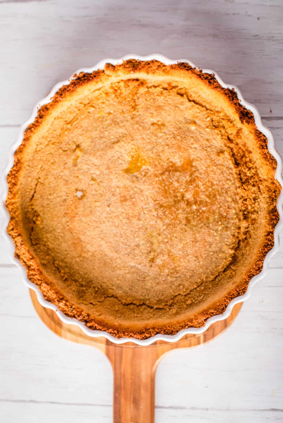  Overhead view of baked graham cracker crust placed on a pie pan. 