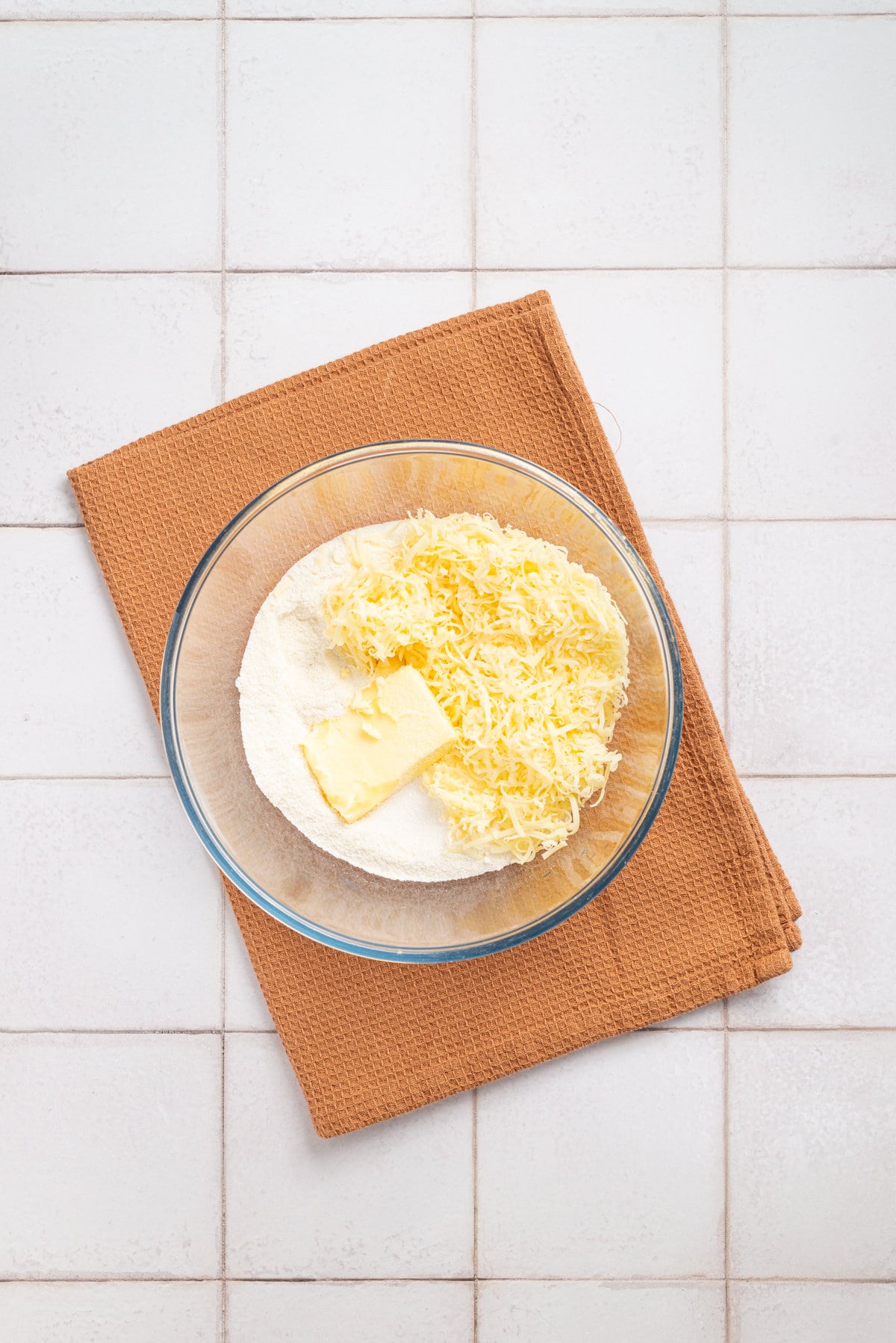 An overhead image of masarepa flour, salt, sugar, butter, and shredded mozzarella cheese.