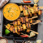 An overhead image of authentic tofu satay on a grill pan with peanut sauce on the side.