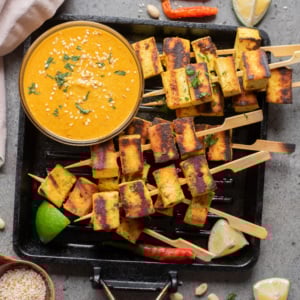 An overhead image of authentic tofu satay on a grill pan with peanut sauce on the side.