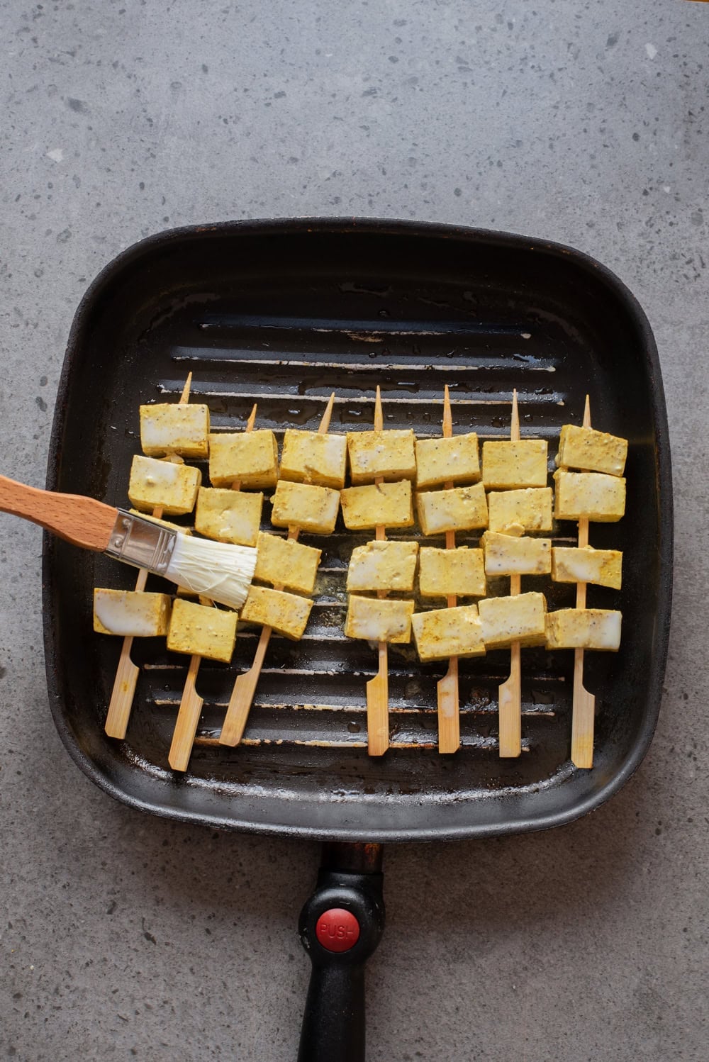 An overhead image of brushing the skewers with neutral oil and placing over grill pan.