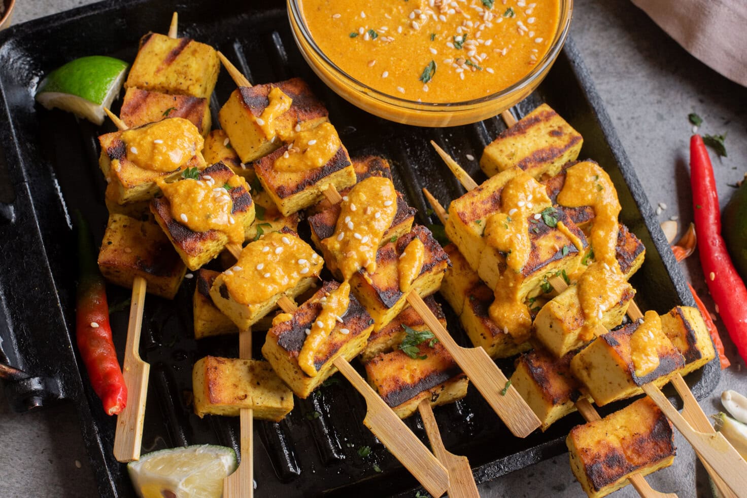 An overhead image of authentic tofu satay on a grill pan with peanut sauce on the side.