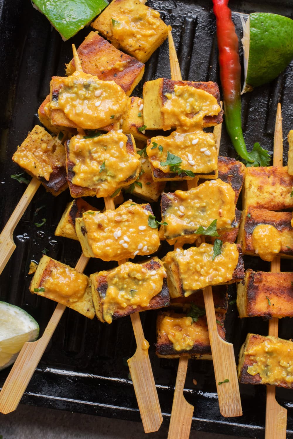 An overhead image of authentic tofu satay on a grill pan with peanut sauce on the side.