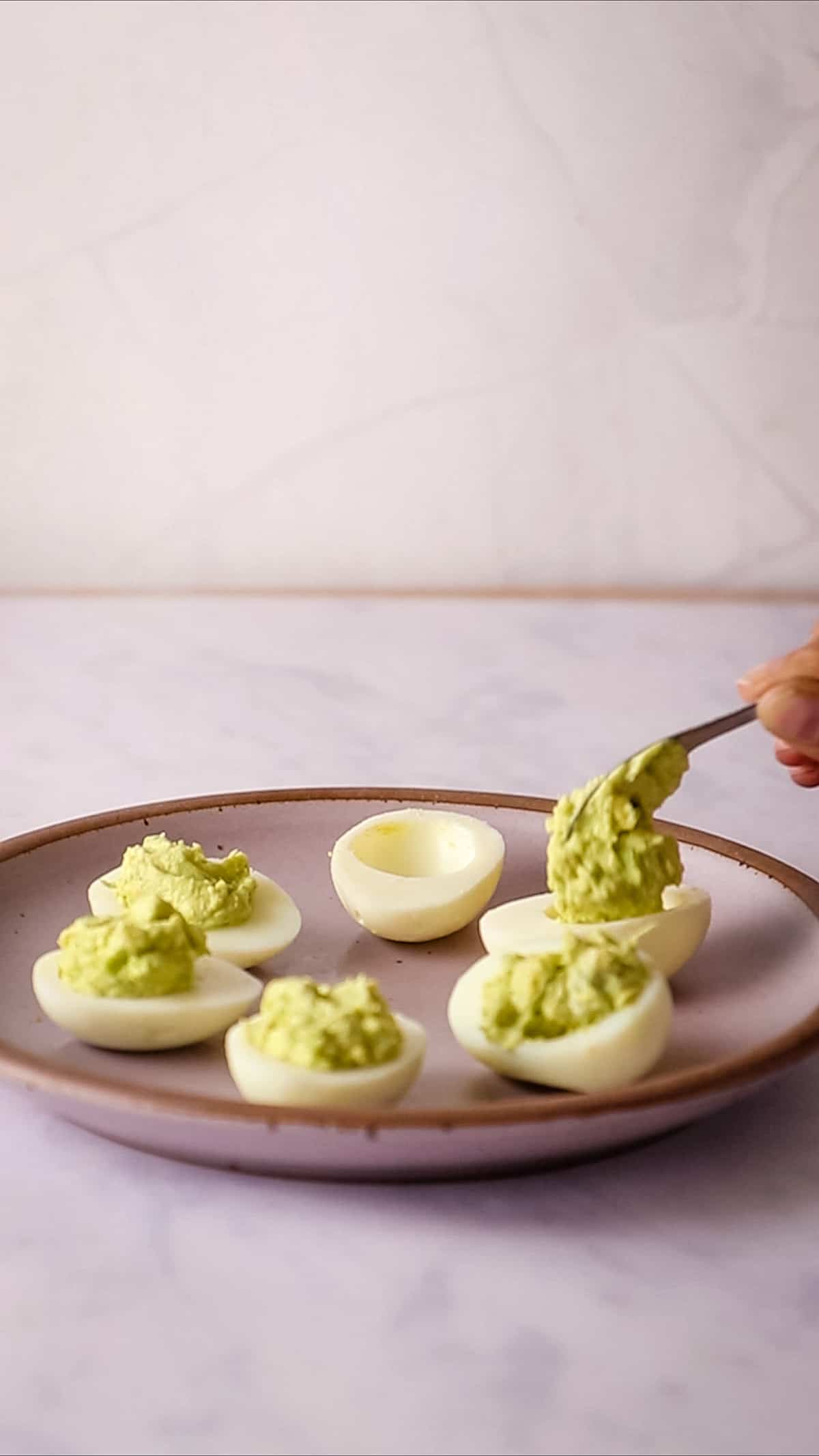 Close up of hand using spoon to fill egg white halves with avocado filling