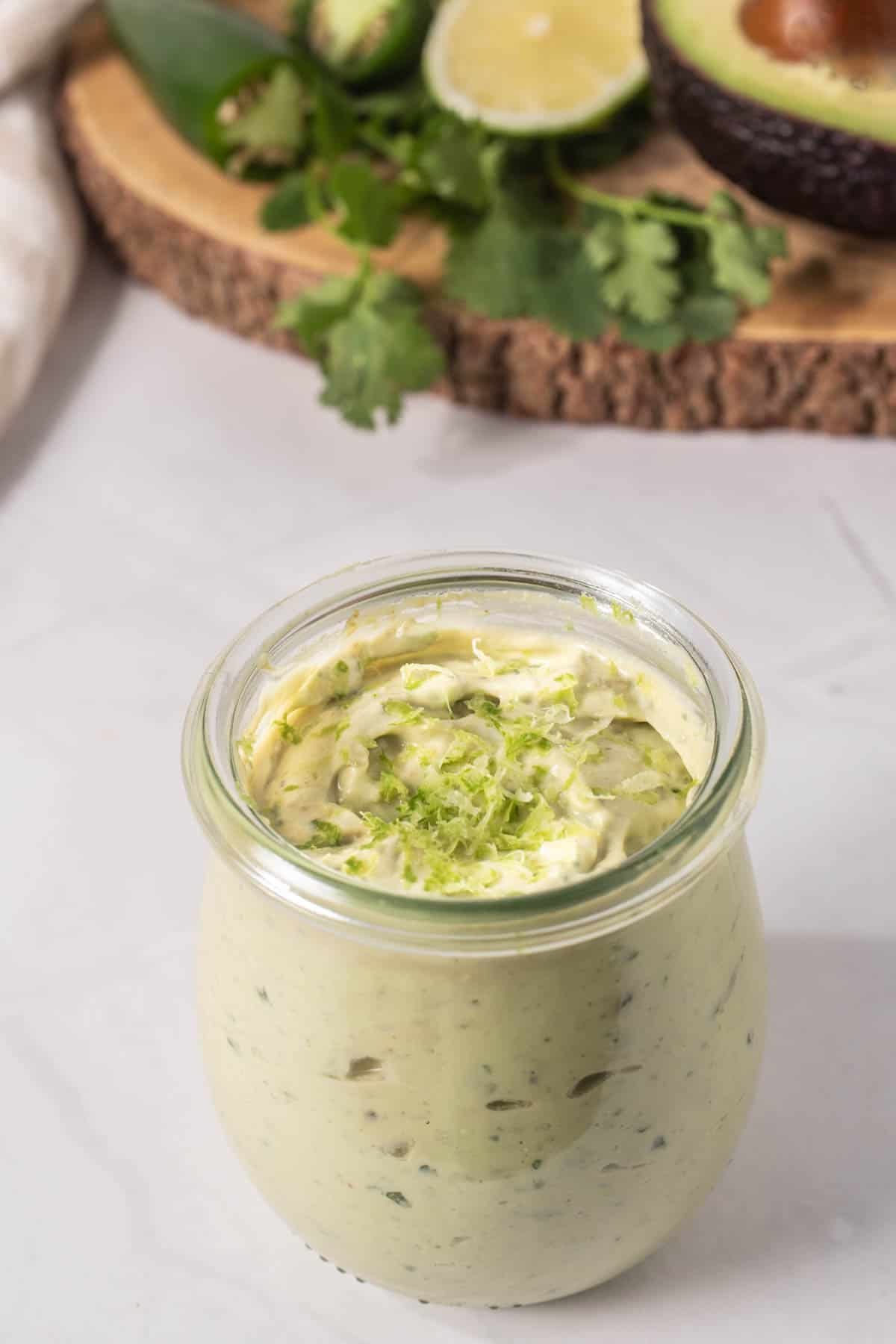 Close up of jar with avocado lime ranch dressing, with ingredients on a wooden platter in the background