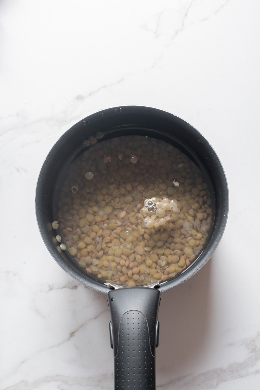 Green lentils cooking in a pot of boiling water.