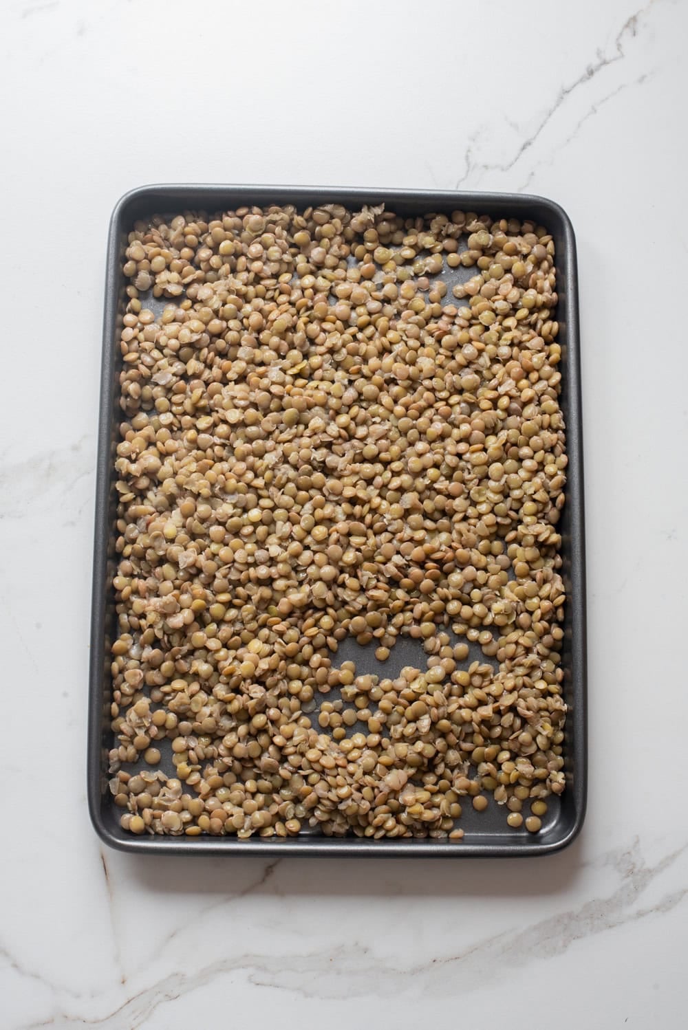 Cooked lentils spread on a tray to cool.