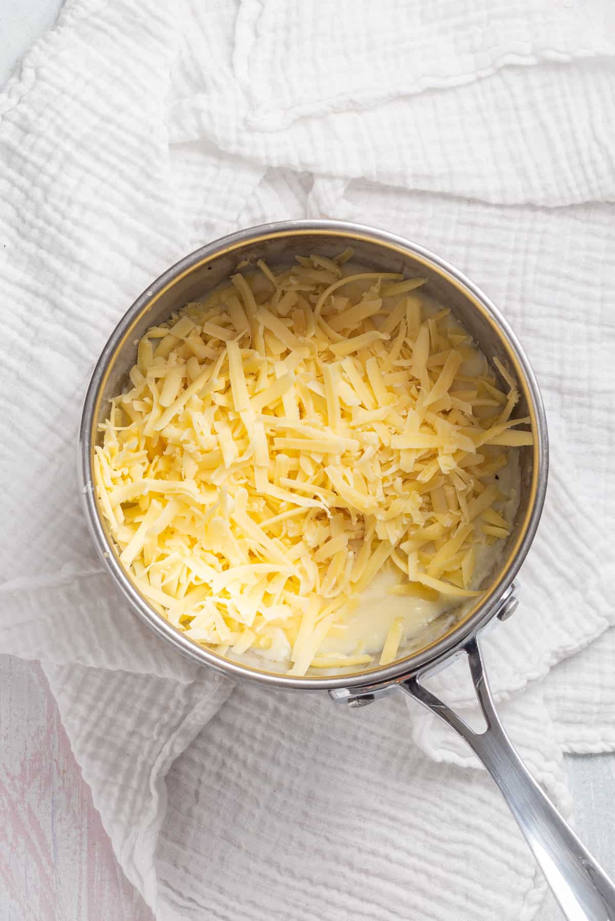 An overhead image of cheese added to the mornay sauce mixture.