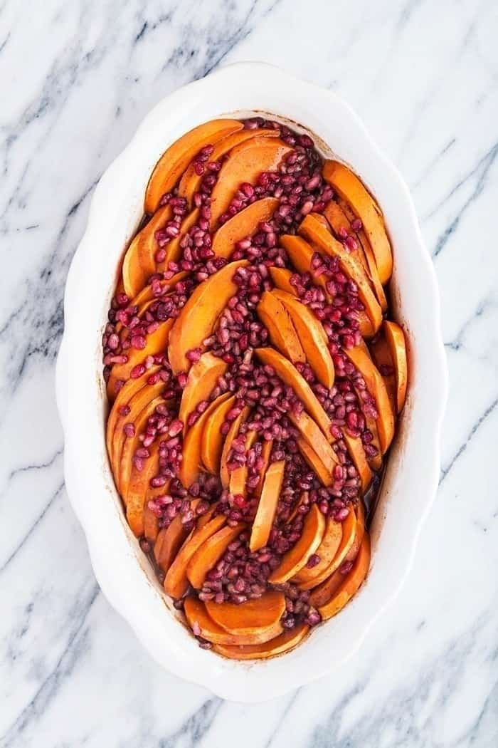 Overhead view of easy-sliced sweet potatoes placed on a white casserole with pomegranate on top.