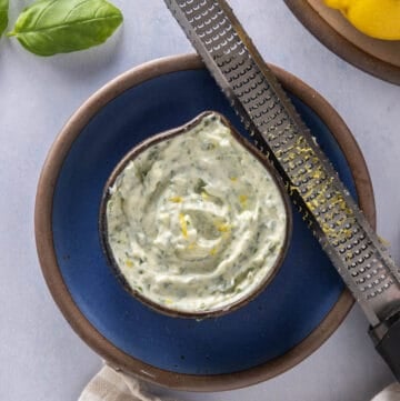 Close up of jar of basil aioli on a blue plate with a microplane / lemon zest resting on a blue plate
