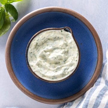 Close up of basil mayo in a jar, on a blue plate, basil in the background