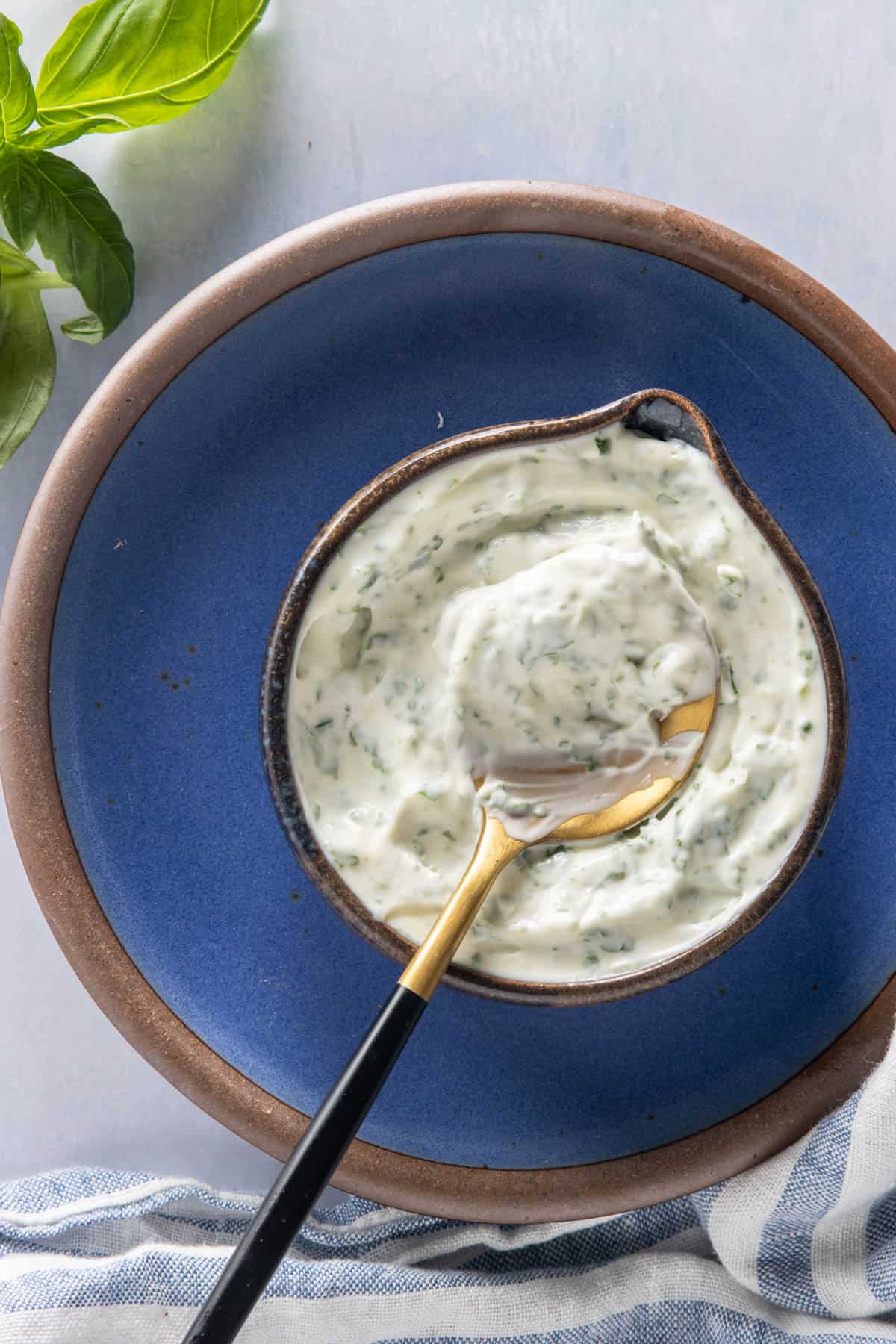 Basil mayonnaise in a jar with a spoon on it, placed on a blue plate