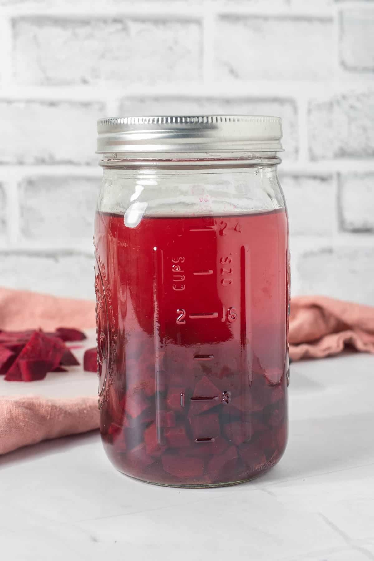 Large mason jar of beet kvass with sliced beets in background
