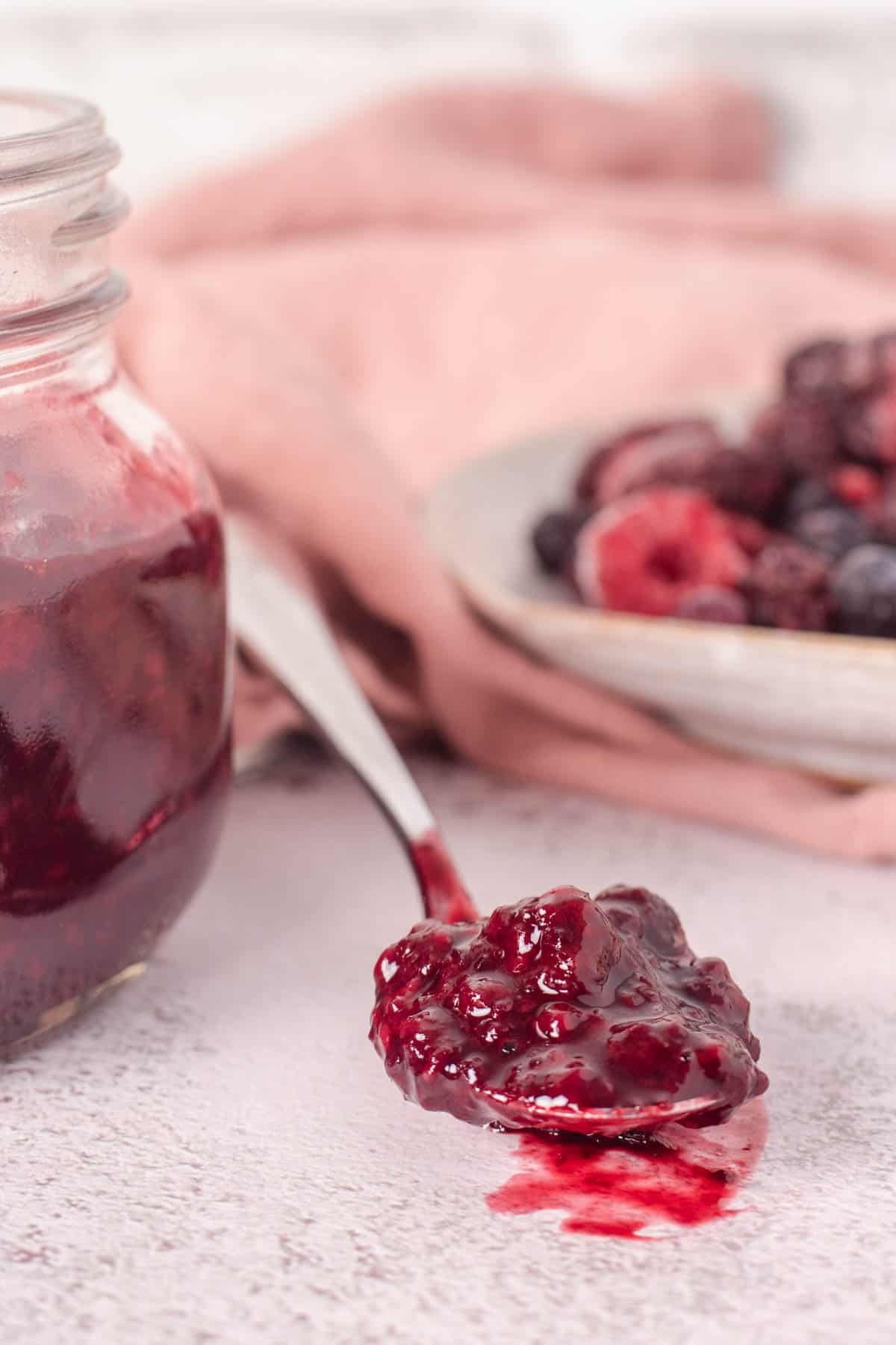 Spoonful of berry compote on the counter, showing consistency - jar of compote and frozen berries in background