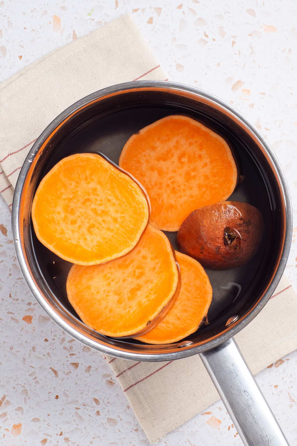 An overhead image of sweet potatoes in a pot with boiling water.