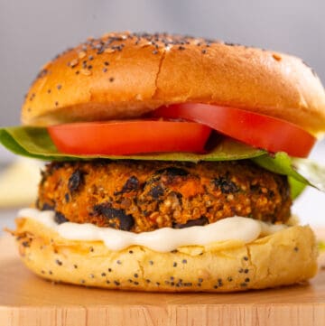 A close up image of a black bean quinoa burger on a chopping board, complete with tomatoes, lettuce, and mayonnaise!