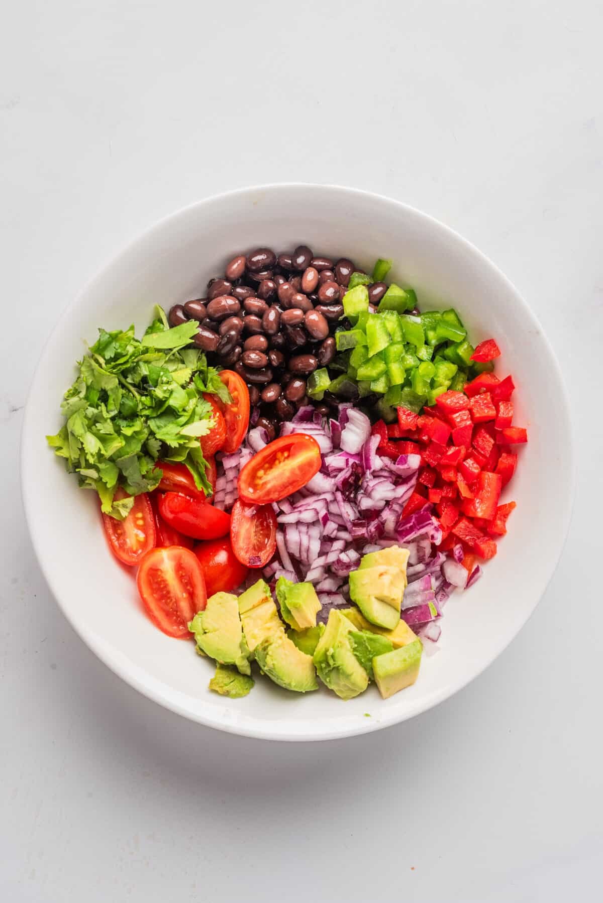 An overhead image of the ingredients of black bean salad together in one bowl, before mixing them together.
