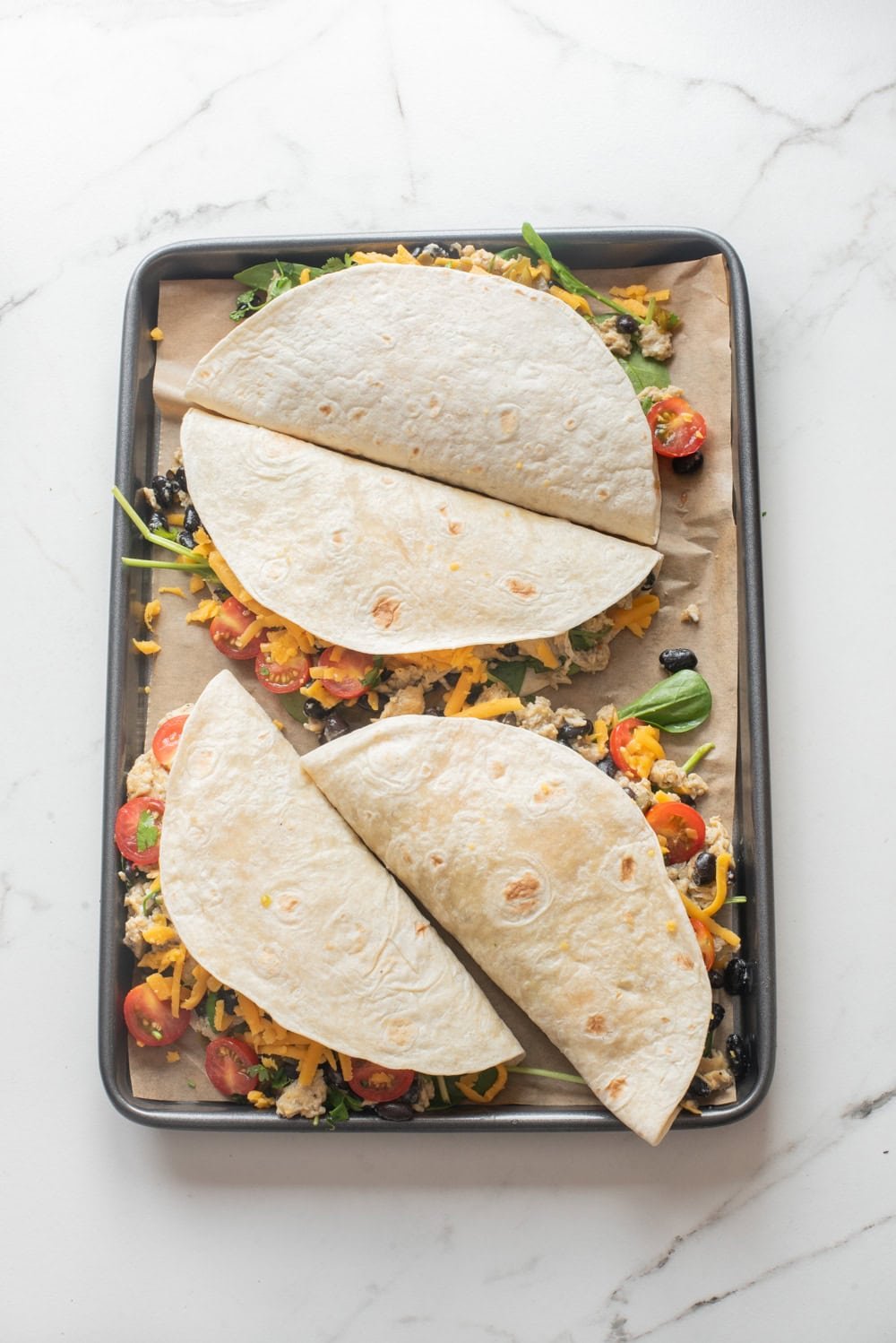 An overhead image of four breakfast quesadillas on a sheet pan, ready to ba baked.
