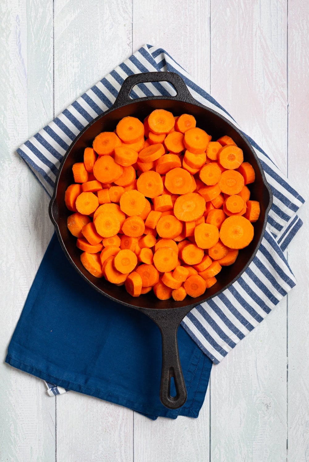 Sliced carrots cooking in a skillet with water, butter, and salt.