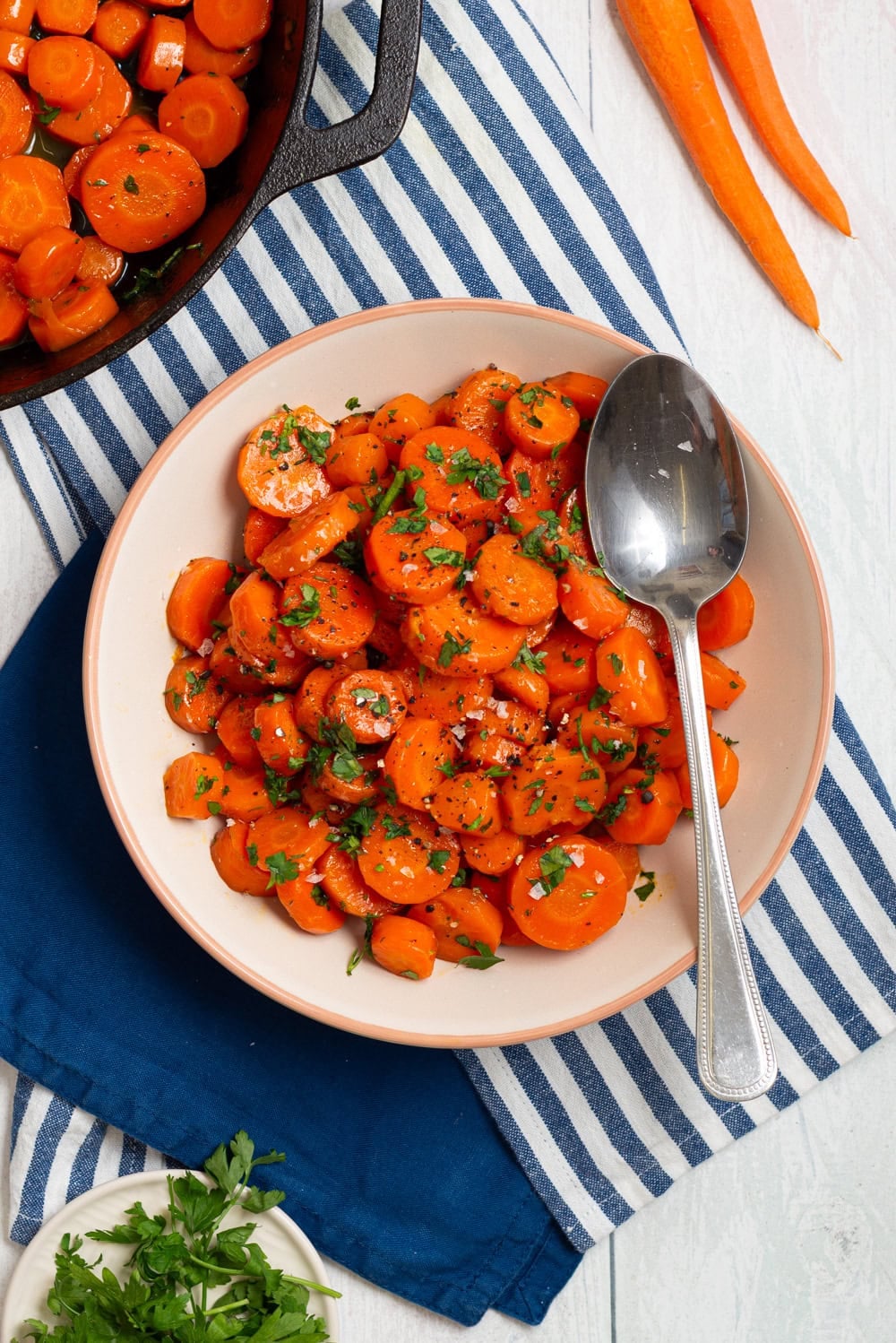 Brown sugar glazed carrots served in a bowl with a spoon and fresh parsley.
