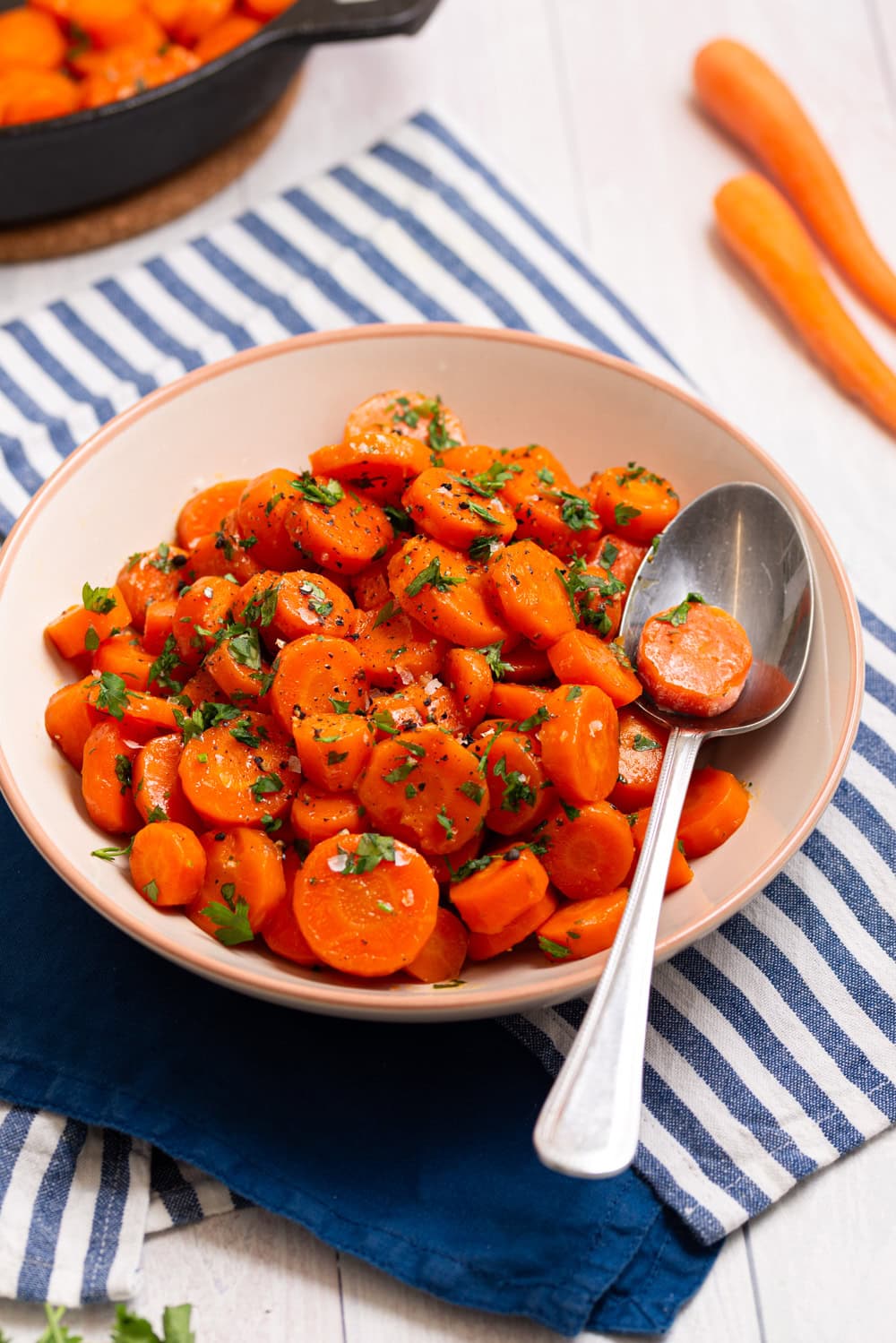 Brown sugar glazed carrots served in a bowl with a spoon and fresh parsley