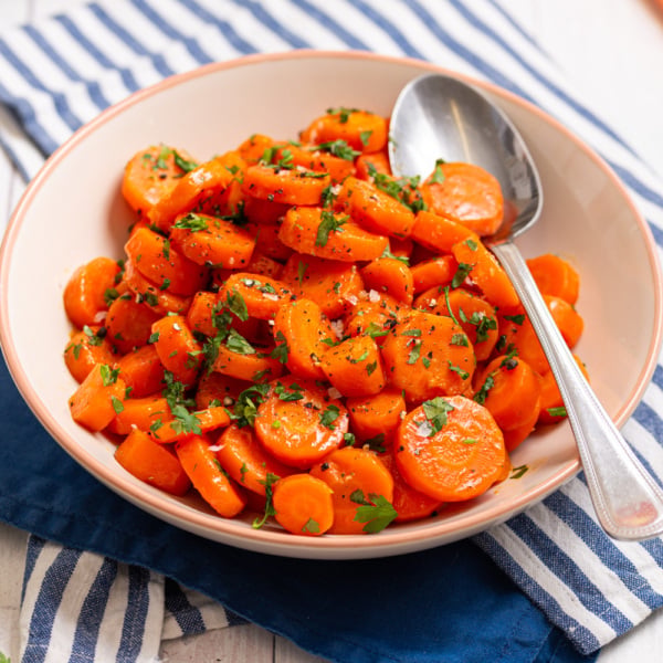 Brown sugar glazed carrots served in a bowl with a spoon and fresh parsley.